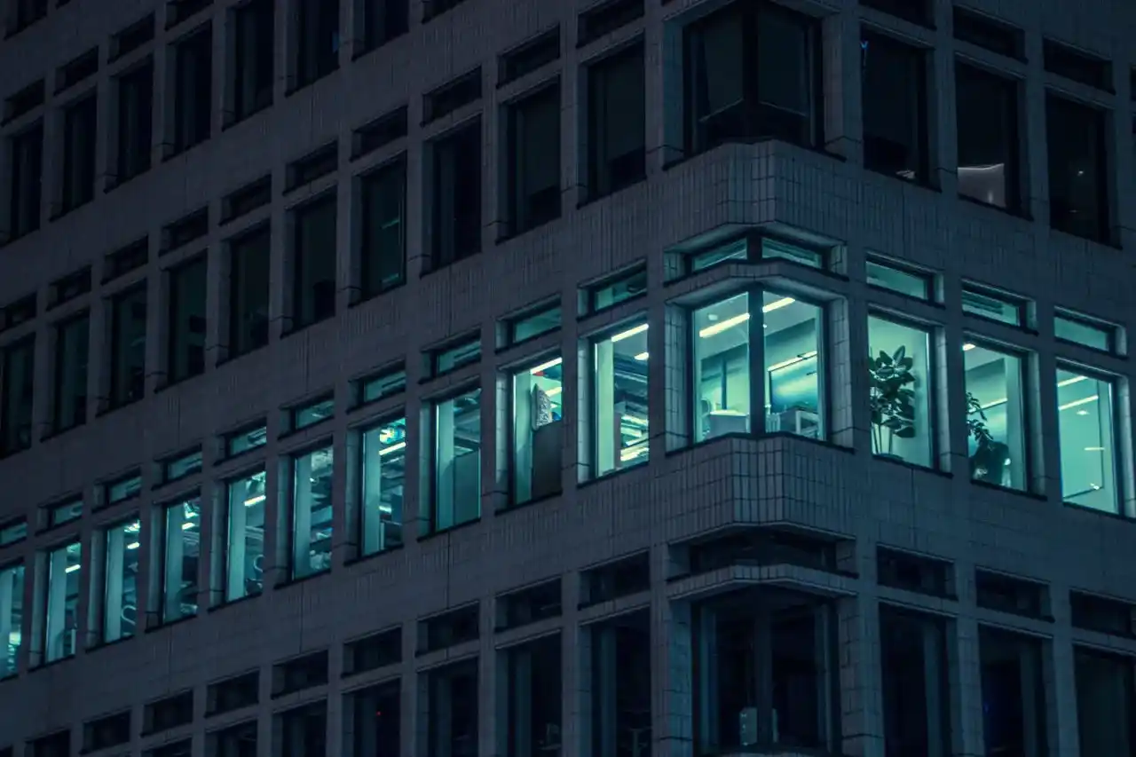 Global Platform Excellence - A sleek, modern glass office tower photographed at dusk with lights on inside, showing multiple floors illuminated. The building should be shot from ground level looking up at an angle, conveying scale and prestige. Look for images of financial district buildings in NYC, London, or Singapore with that blue-hour lighting that suggests late working hours typical of PE/VC culture.